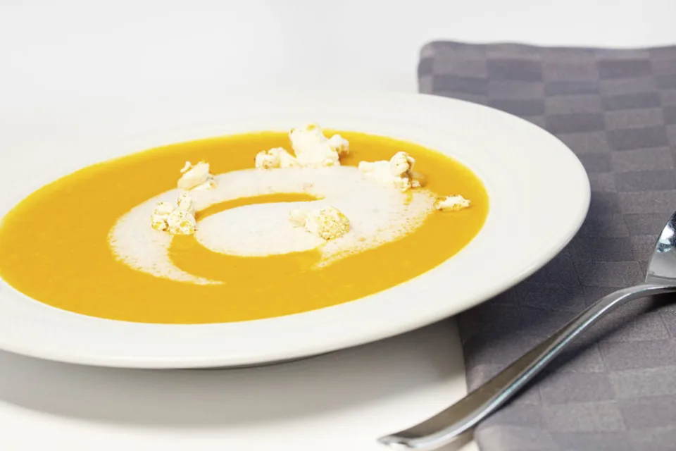 Orangefarbene Cremesuppe mit Schaum und Käse im tiefen Teller